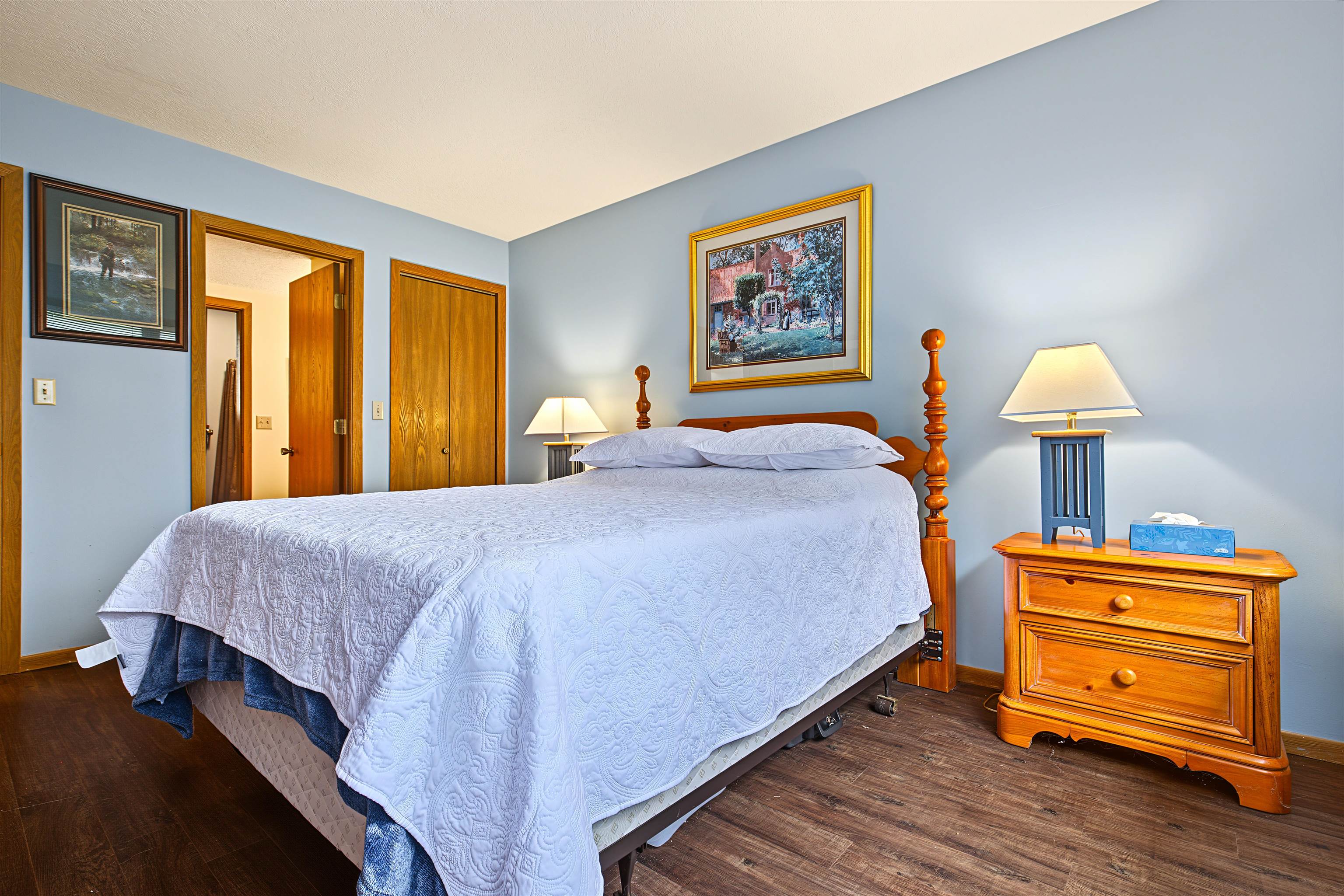Furnished bedroom with a white-quilted four-poster bed and wooden bedside chest.