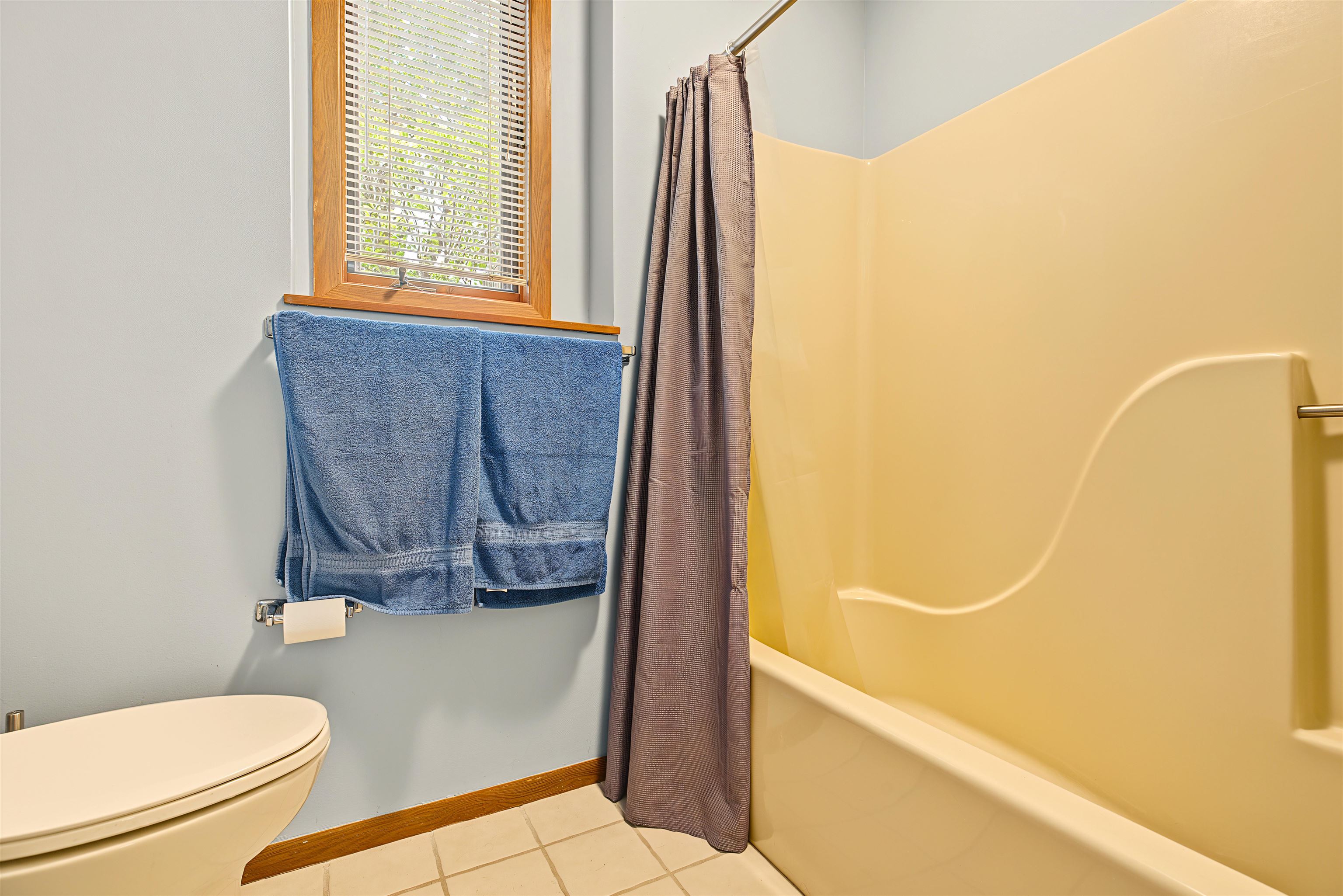 Bathroom with a cream bathtub, blue towels, and a wood-trimmed window.