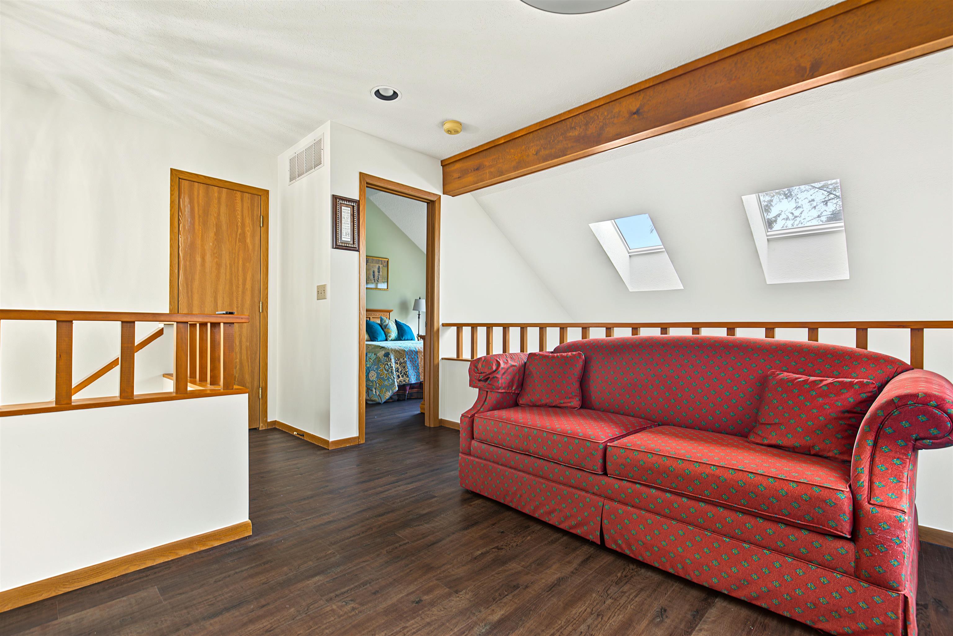 Upper-level sitting area with a red patterned sofa, skylights, and an adjoining bedroom.