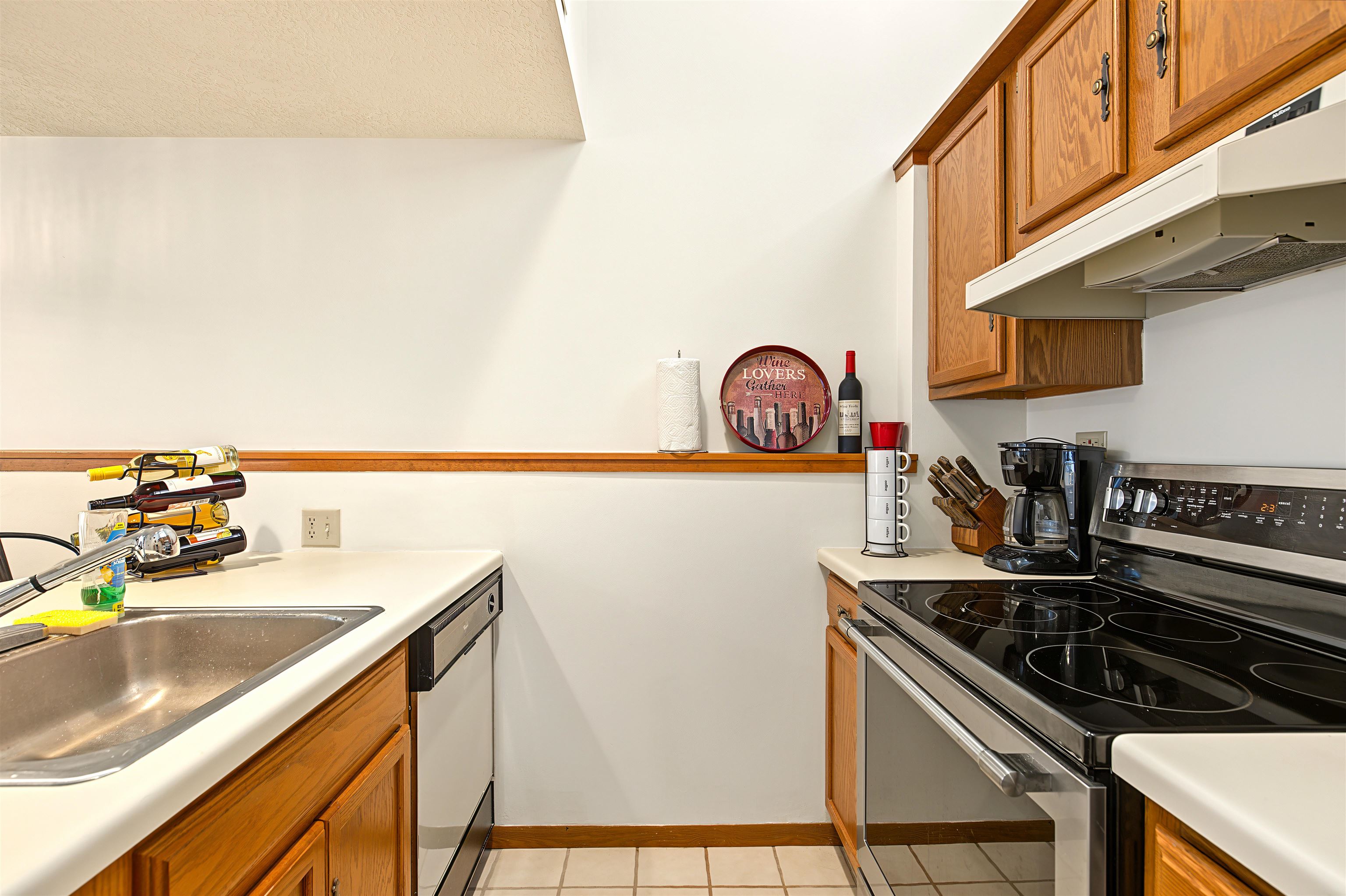 Kitchen with oak cabinets, white countertops, stainless-steel sink, and black glass-top range.