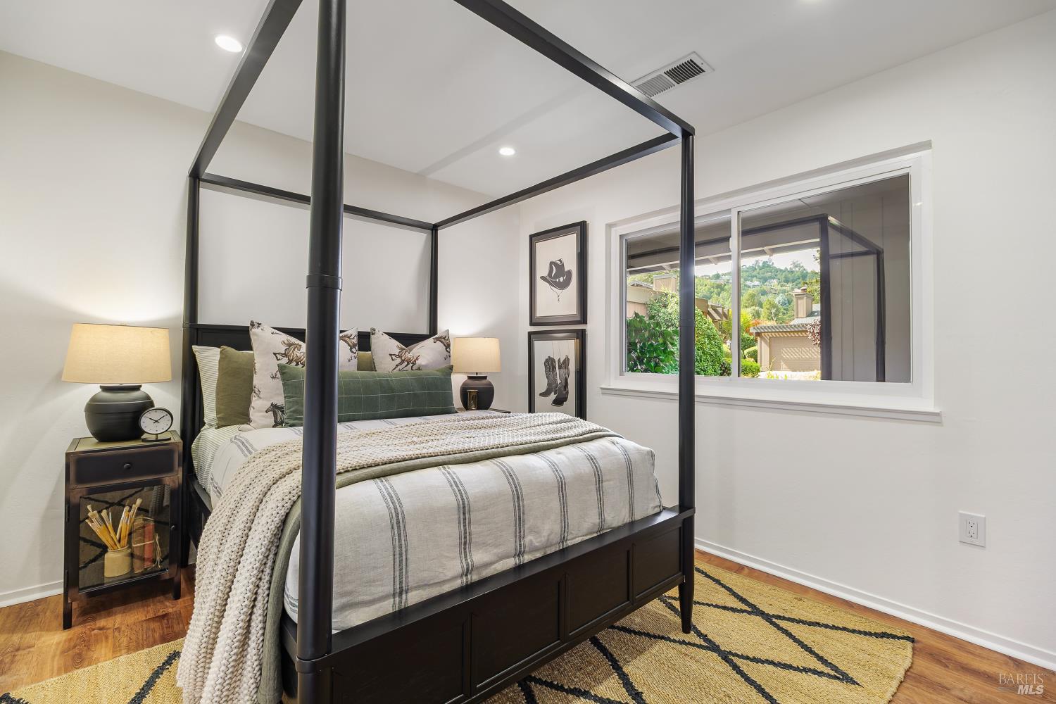 Staged bedroom with a dark four-poster bed, striped bedding, and a large garden-view window.