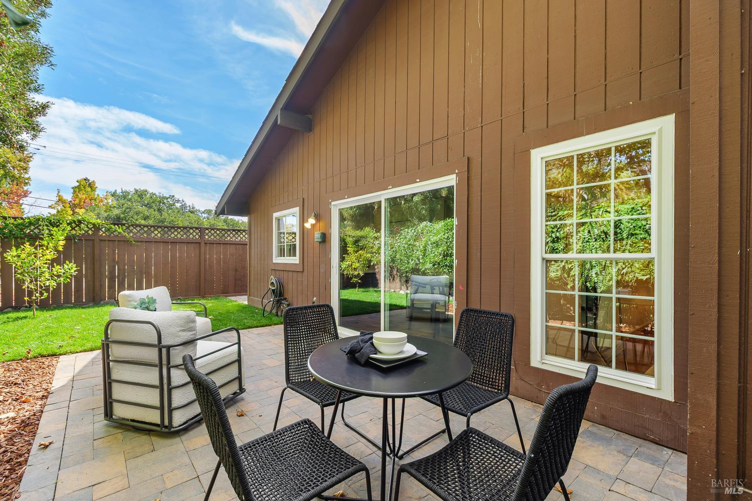 Backyard patio with wicker dining chairs, a sliding glass door, and a fenced lawn.