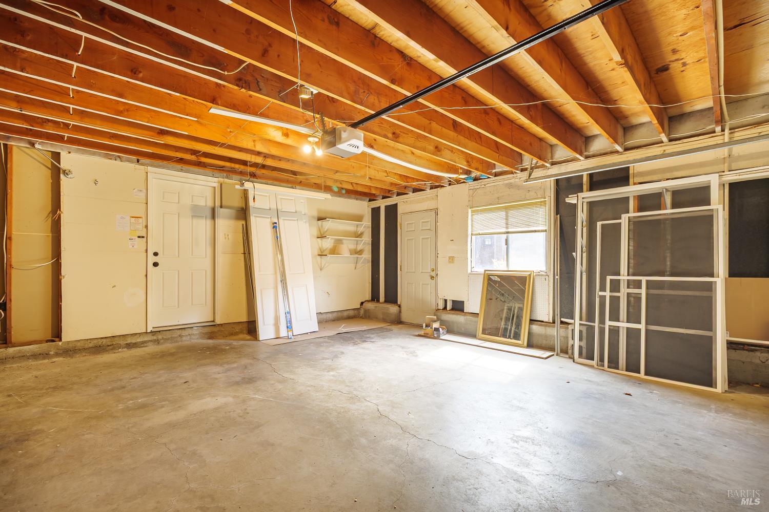Vacant garage with exposed wood ceiling beams and window screens leaning against the wall.