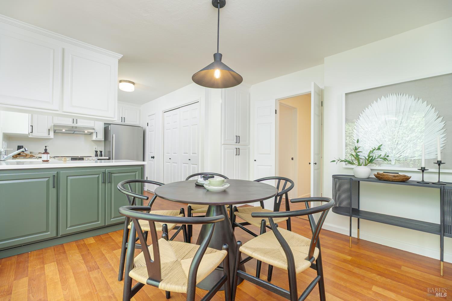 Kitchen and dining area with sage-green cabinets, a round table, and woven-seat chairs.