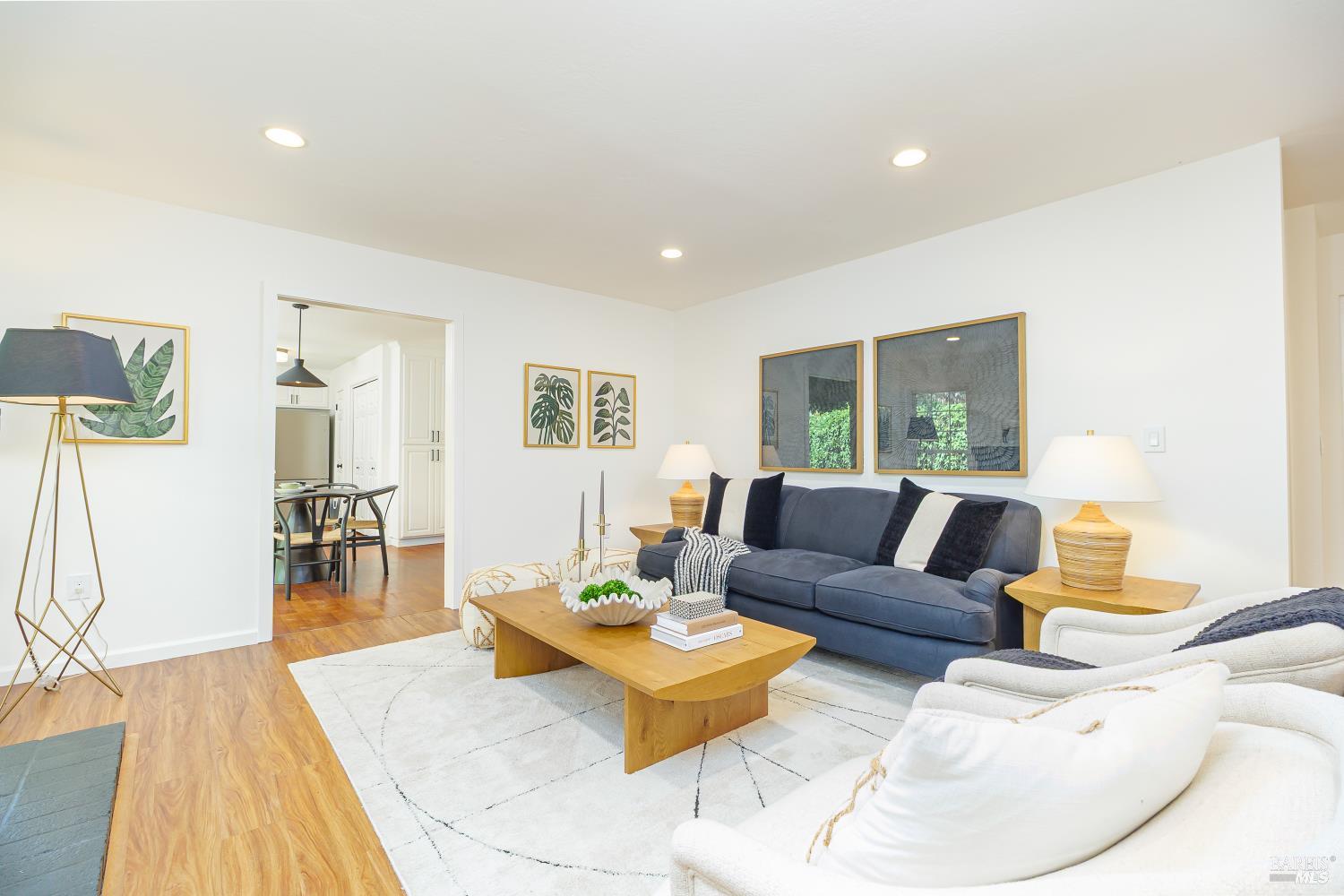 Staged living room with a blue sofa, white armchairs, and a view into the dining area.