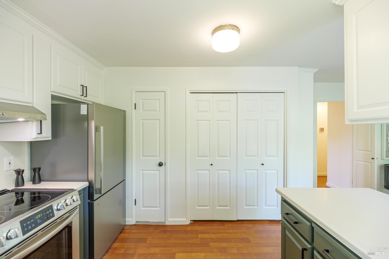 Kitchen with white cabinets, stainless steel appliances, and warm hardwood floors.