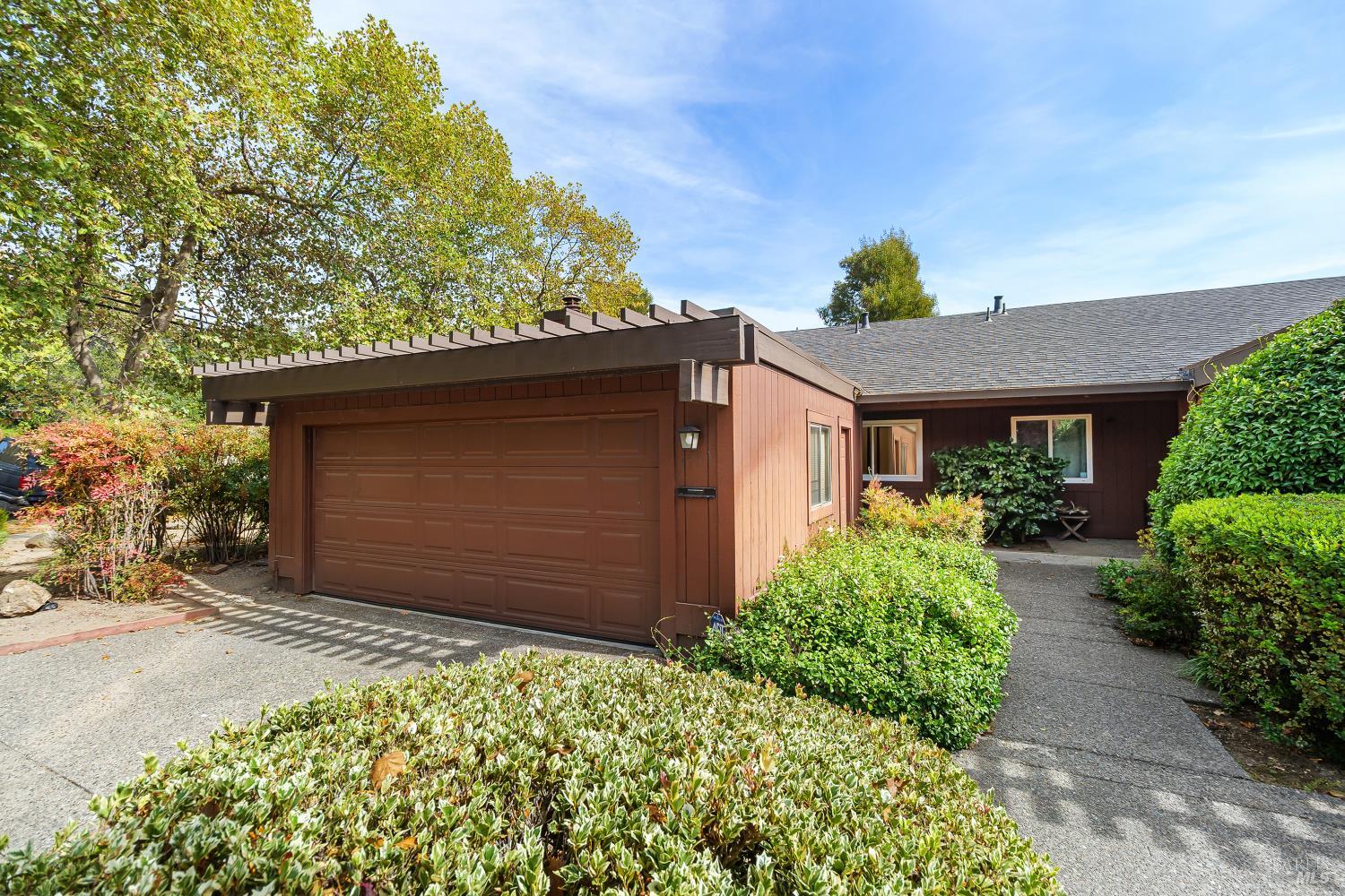 Brown single-story home with a large garage, pergola-style overhang, and landscaped front walkway.