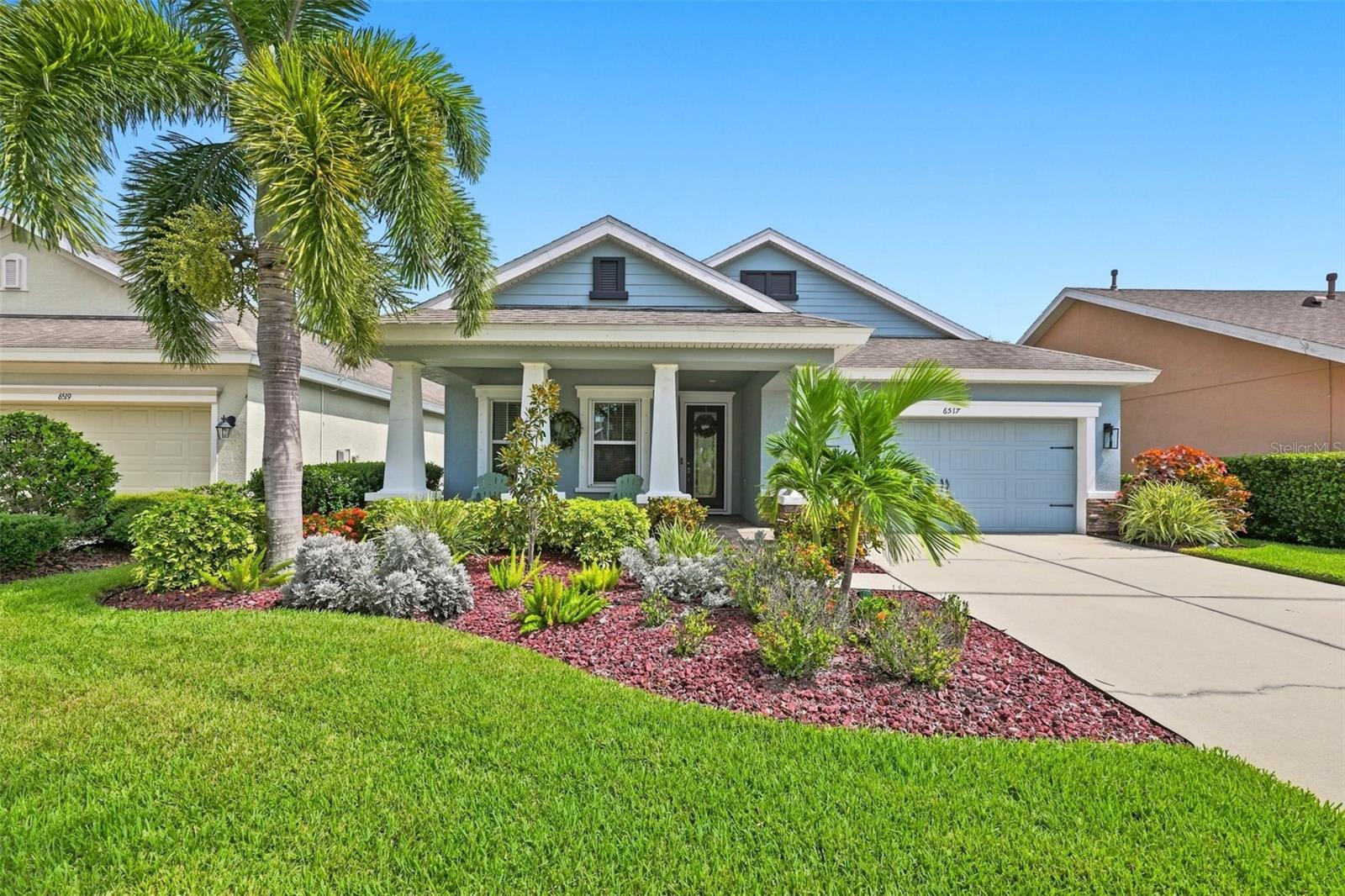 Florida home with a covered porch, attached garage, palm trees, and colorful front landscaping.
