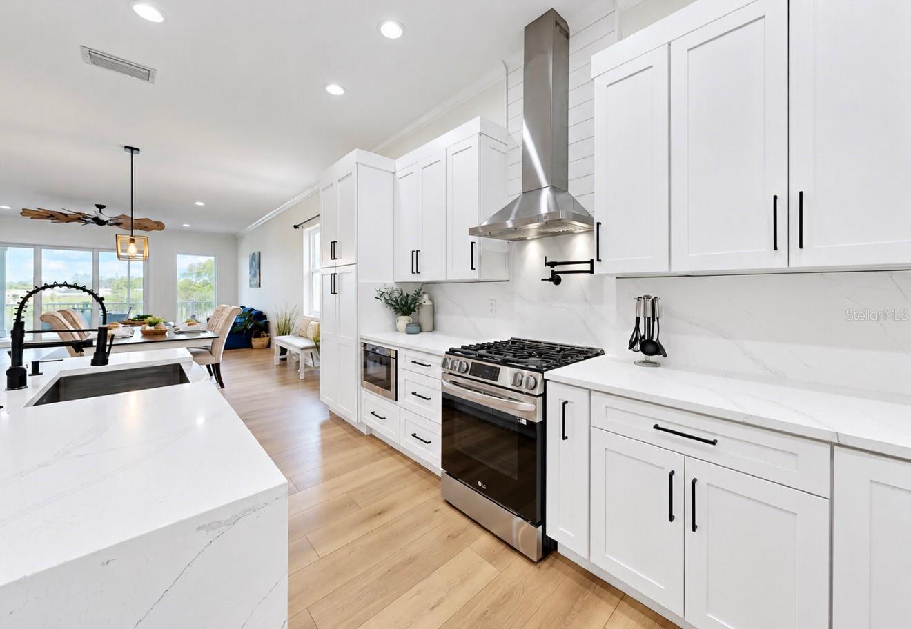 Bright white kitchen with a large island, stainless steel range, and water visible beyond the dining area.