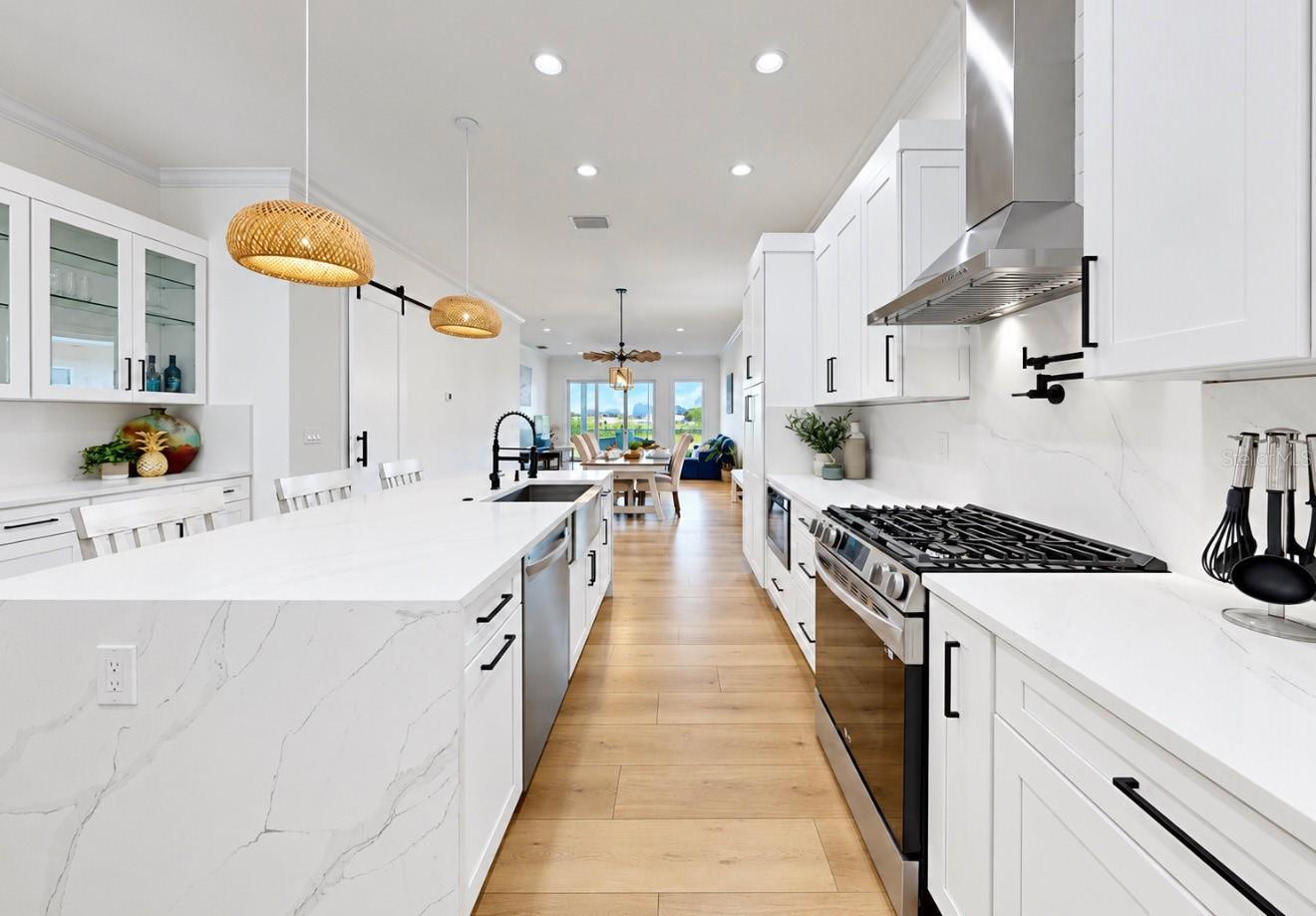 Bright white kitchen with a veined stone island, stainless steel range, and woven pendant lights.