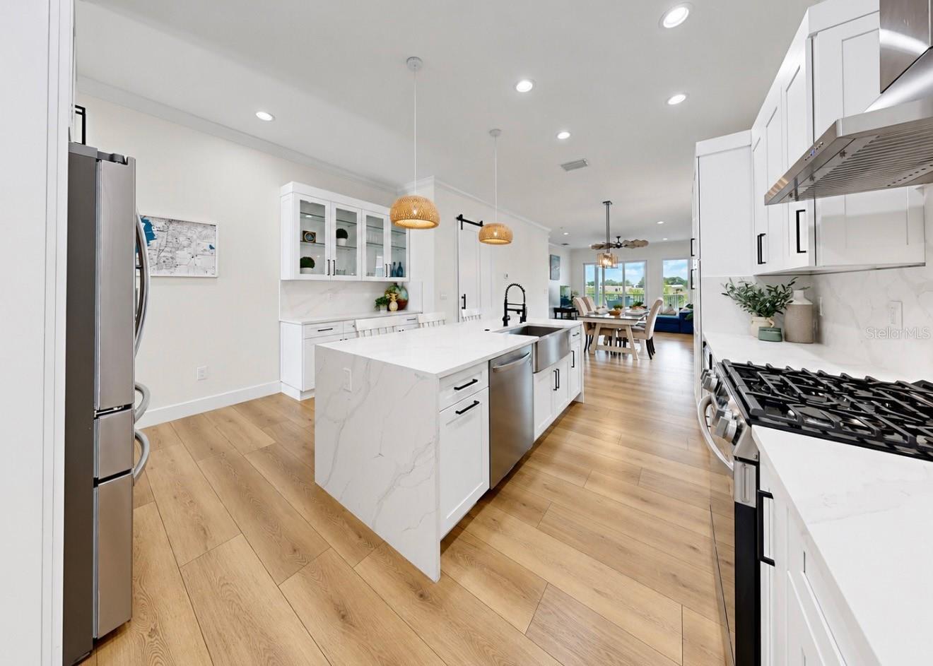 Bright white kitchen with a waterfall island, stainless steel appliances, and light wood floors.