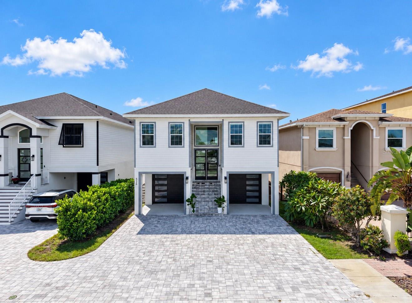 Two-story white home with twin black garage doors and a wide paver driveway.