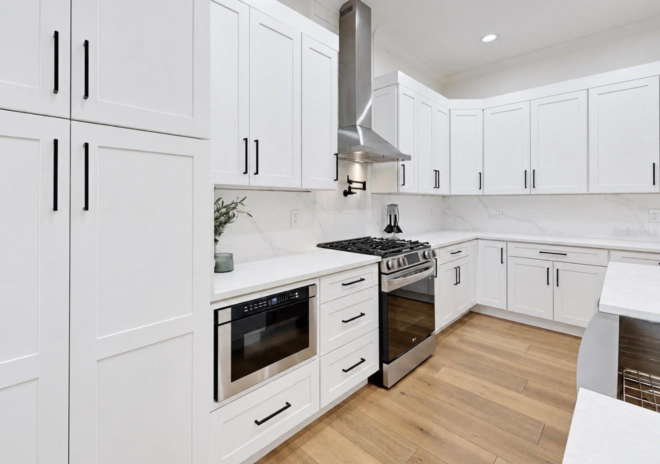 Modern kitchen with white shaker cabinets, stainless steel appliances, and light wood flooring.
