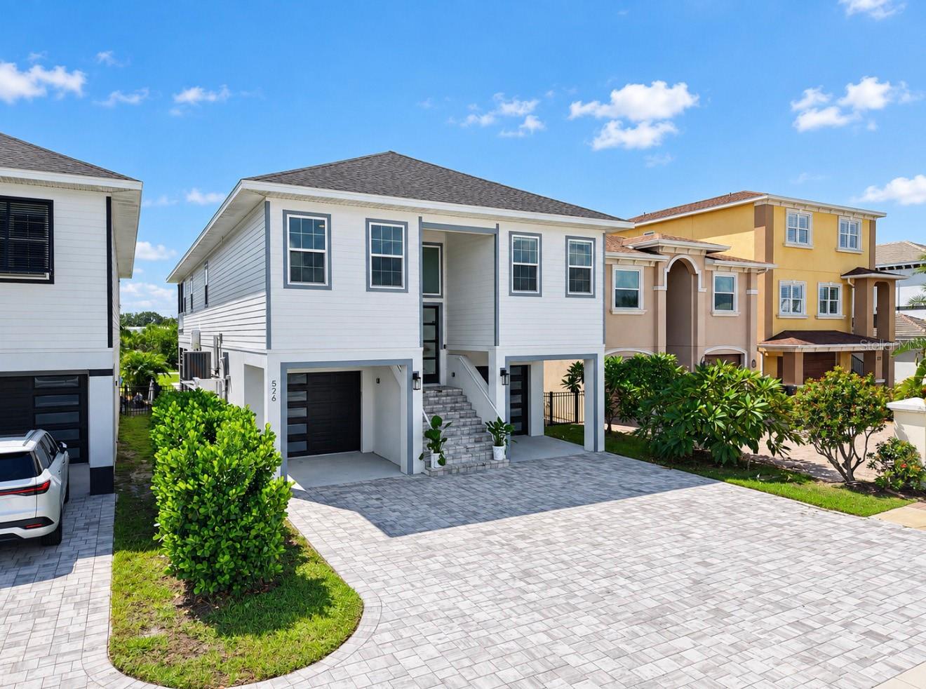 Modern white two-story house with gray trim, two garage doors, and a wide paved driveway.