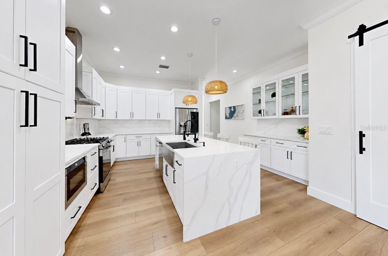 Modern white kitchen with a large marble-look island, black fixtures, and warm wood flooring.
