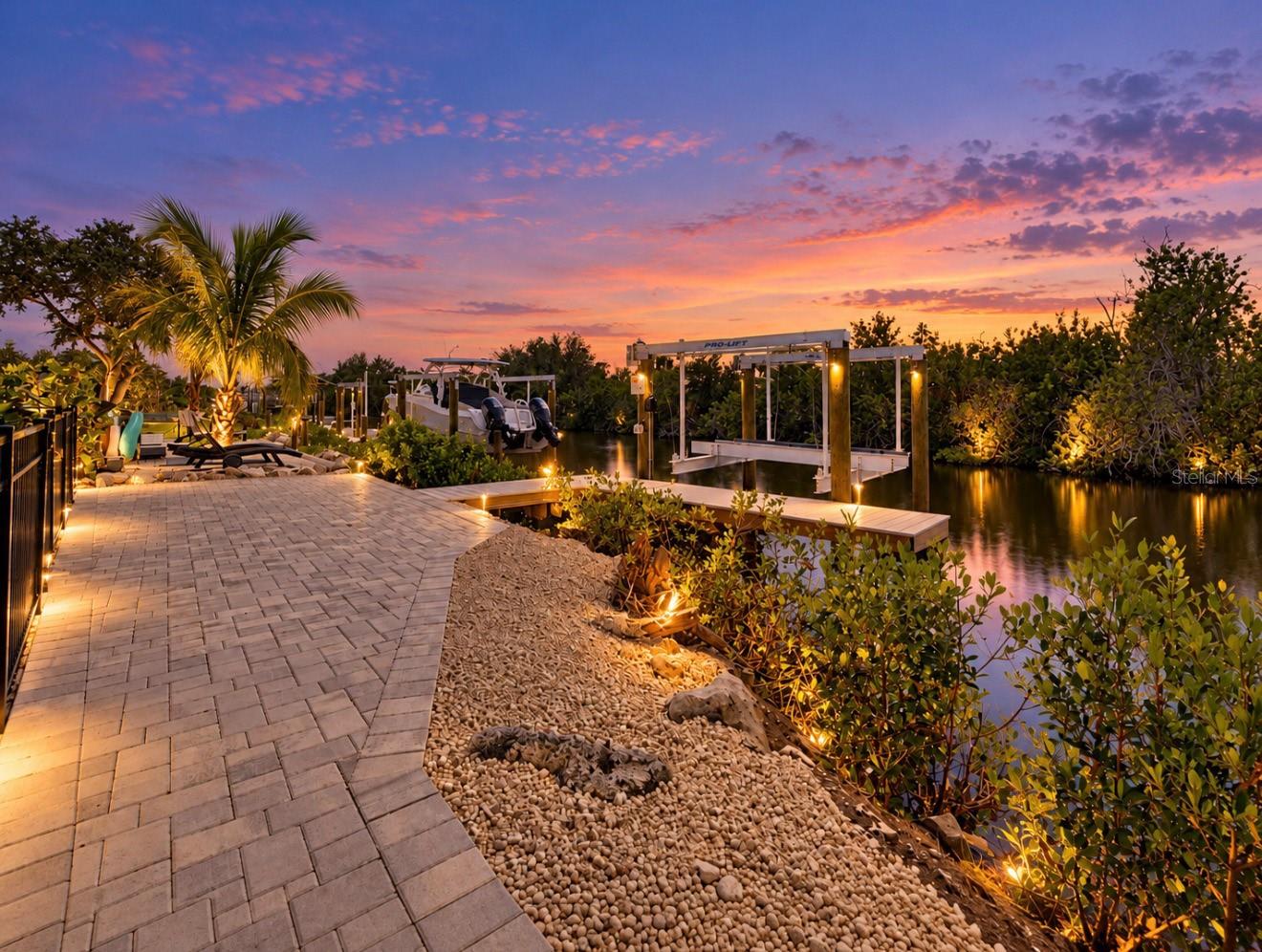 Waterfront patio and private dock with a boat lift beneath a colorful dusk sky.