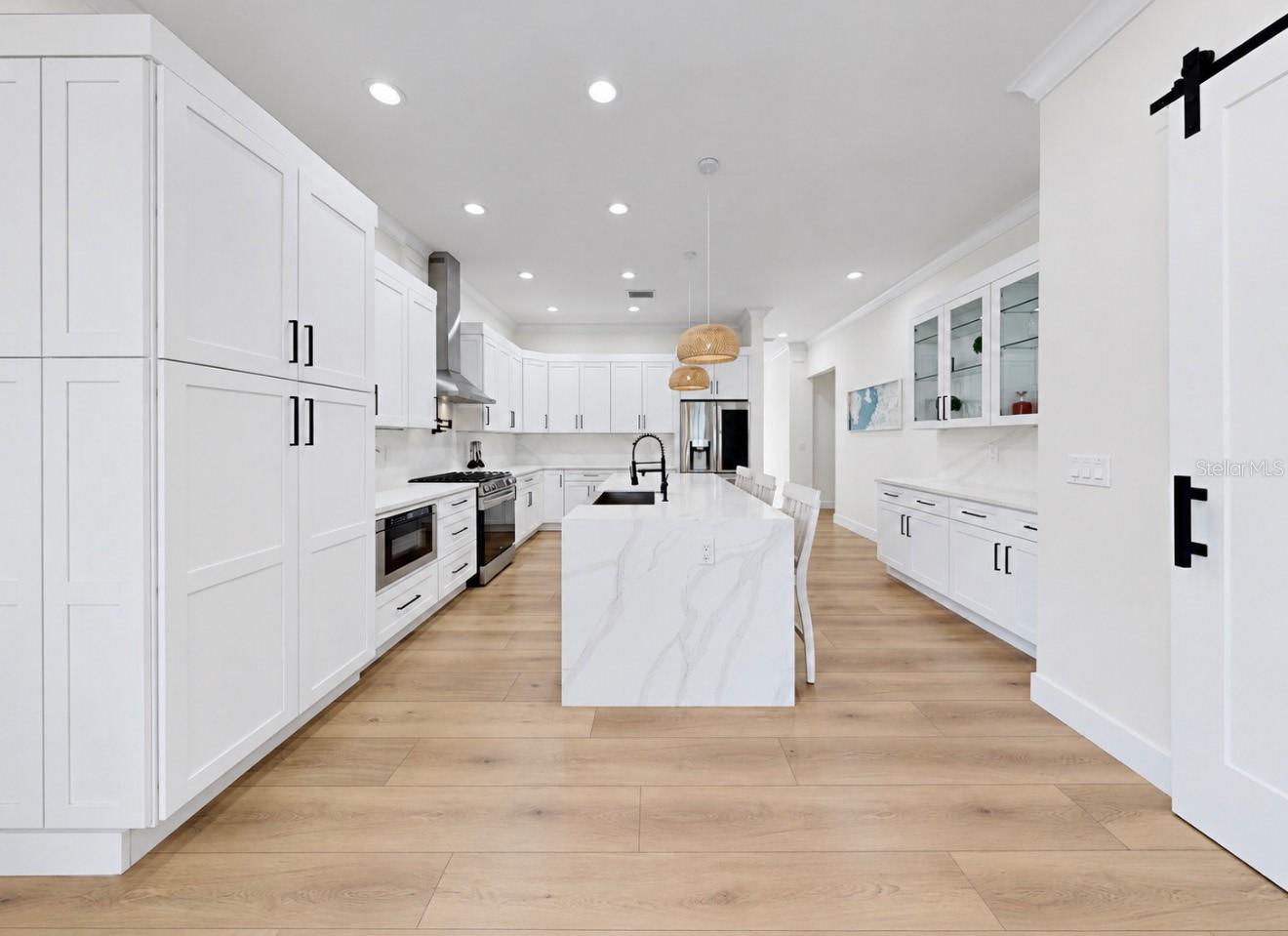 Modern white kitchen with a large marble-look island, stainless steel appliances and light wood floors.