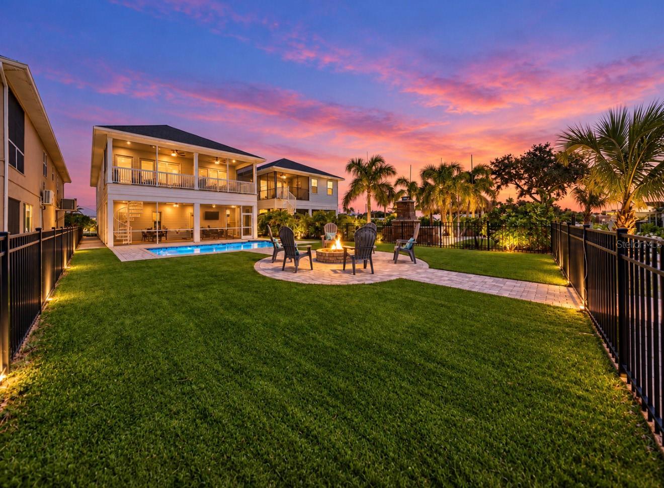 Fenced backyard with a pool and fire pit seating beneath a vivid sunset sky.