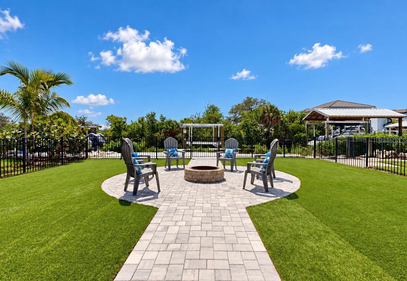 Backyard patio with a stone fire pit, four Adirondack chairs, and a paved walkway through the lawn.
