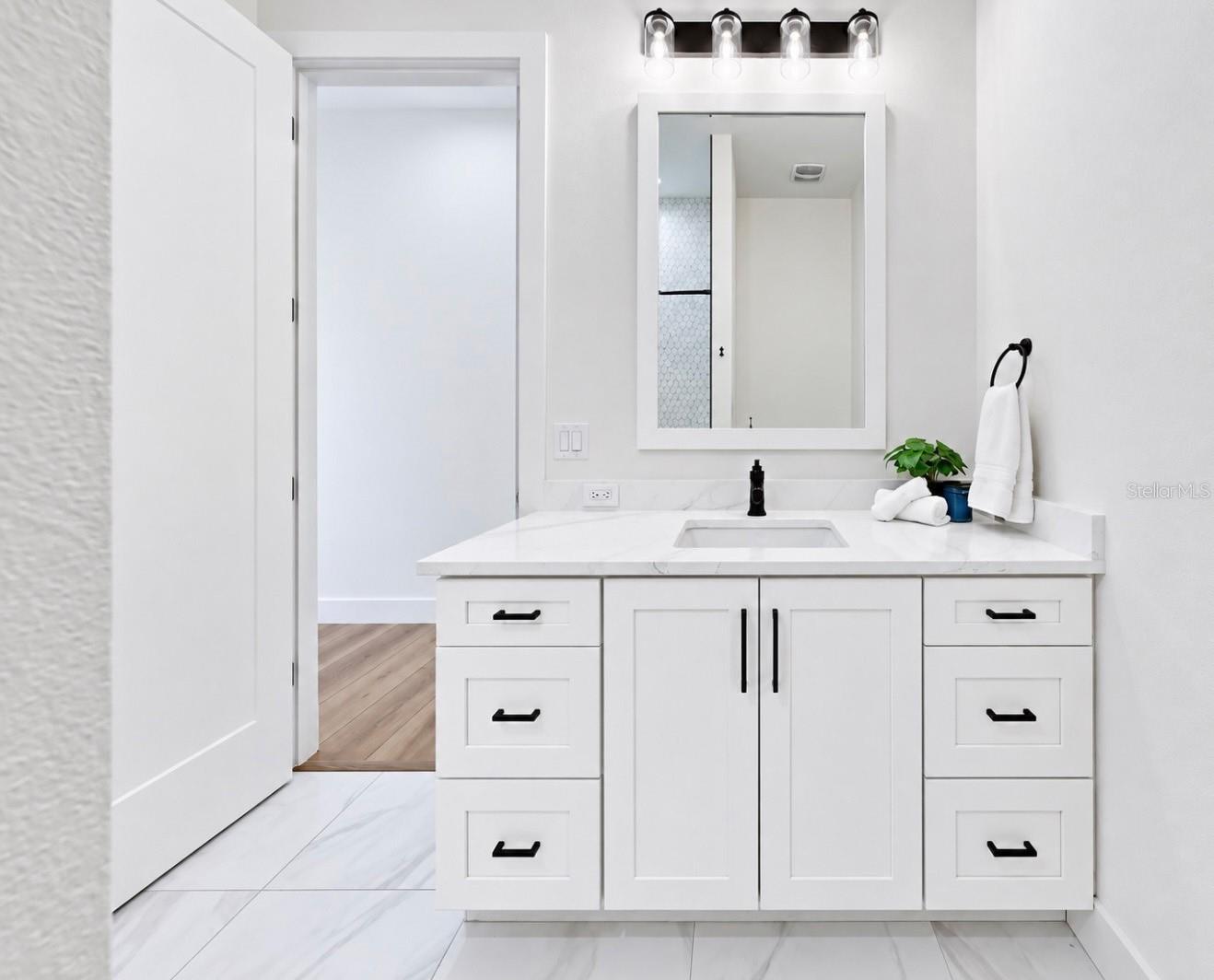Bright bathroom vanity with white cabinetry, a marble-look counter, black fixtures, and a large framed mirror.