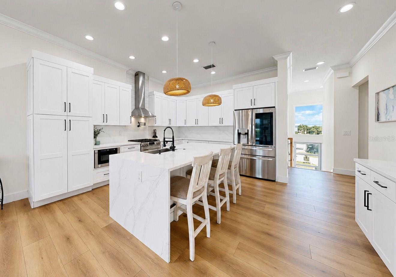 Bright kitchen with white cabinetry, a large island, woven pendant lights, and stainless steel appliances.