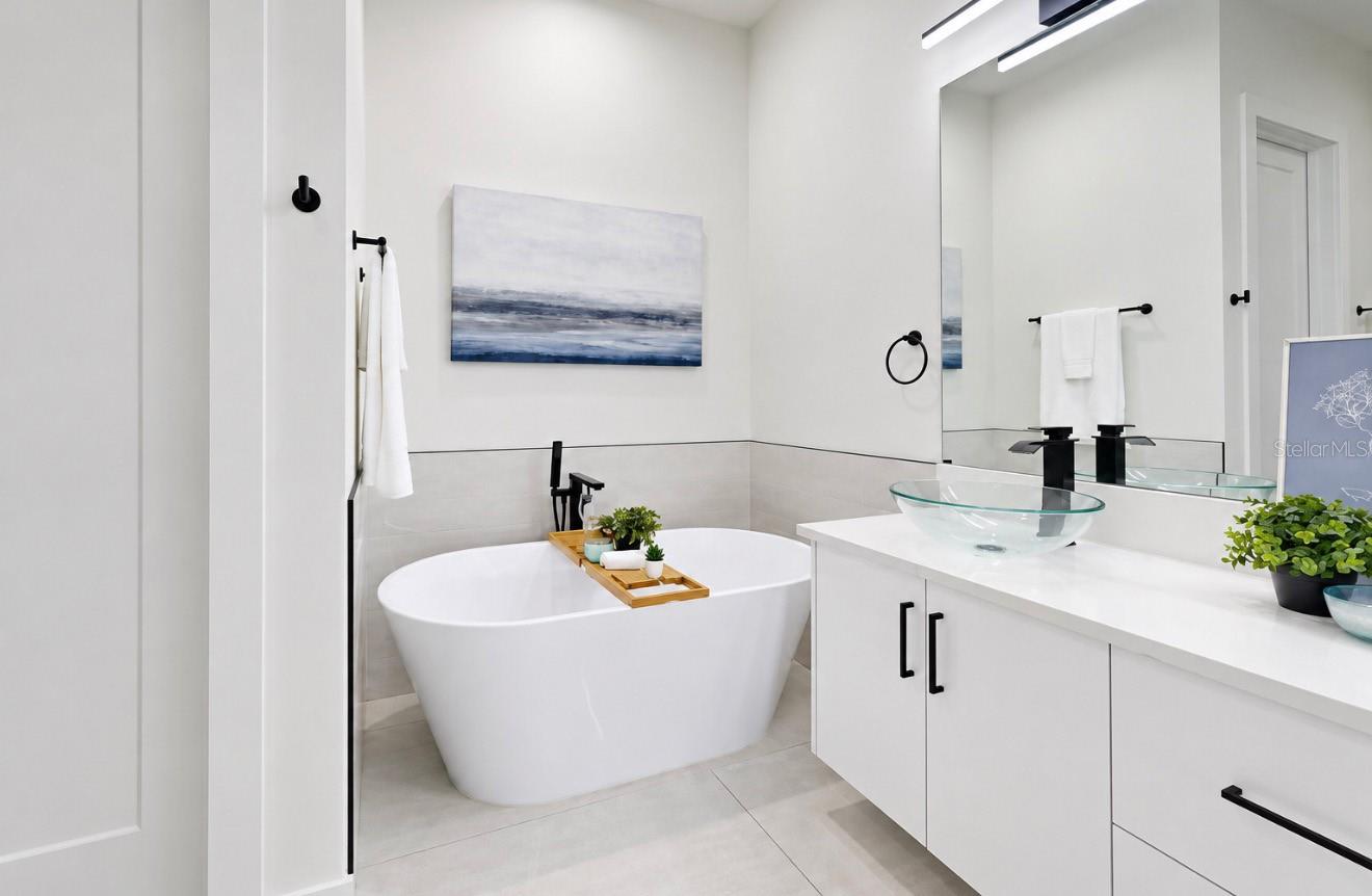 Modern bathroom with a freestanding soaking tub, black fixtures, and a glass vessel sink.
