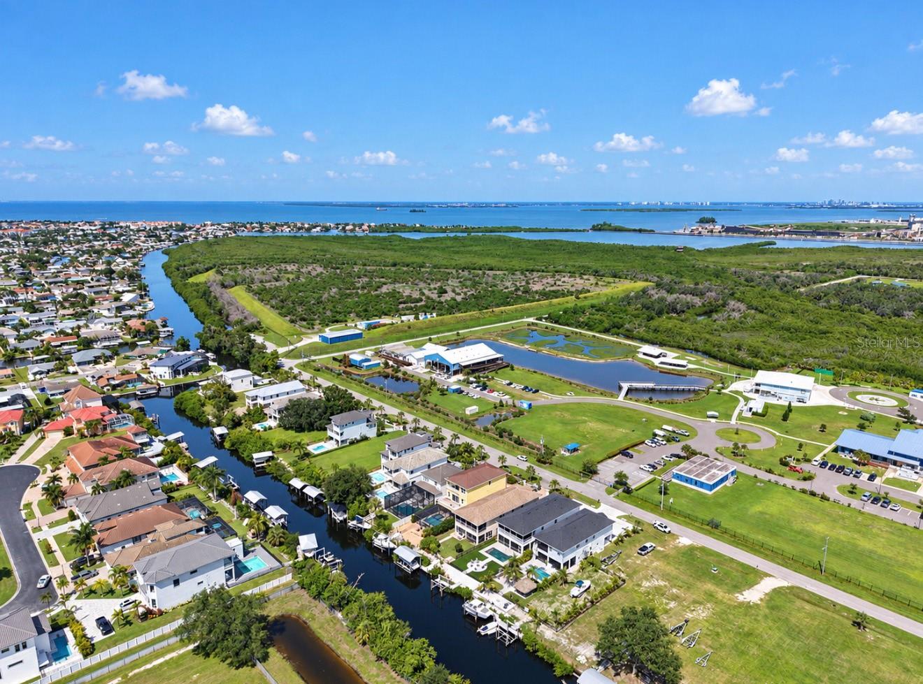 Aerial view of waterfront homes and canals beside green wetlands, with the bay in the distance.