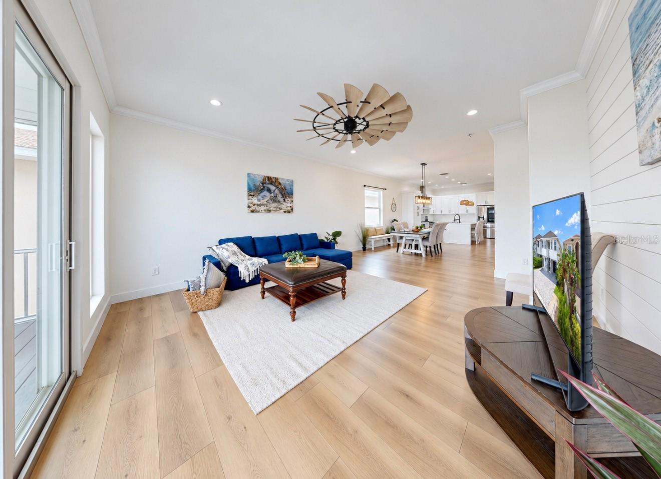 Open-plan living room with a blue sectional, light wood floors, and dining area beside a white kitchen.