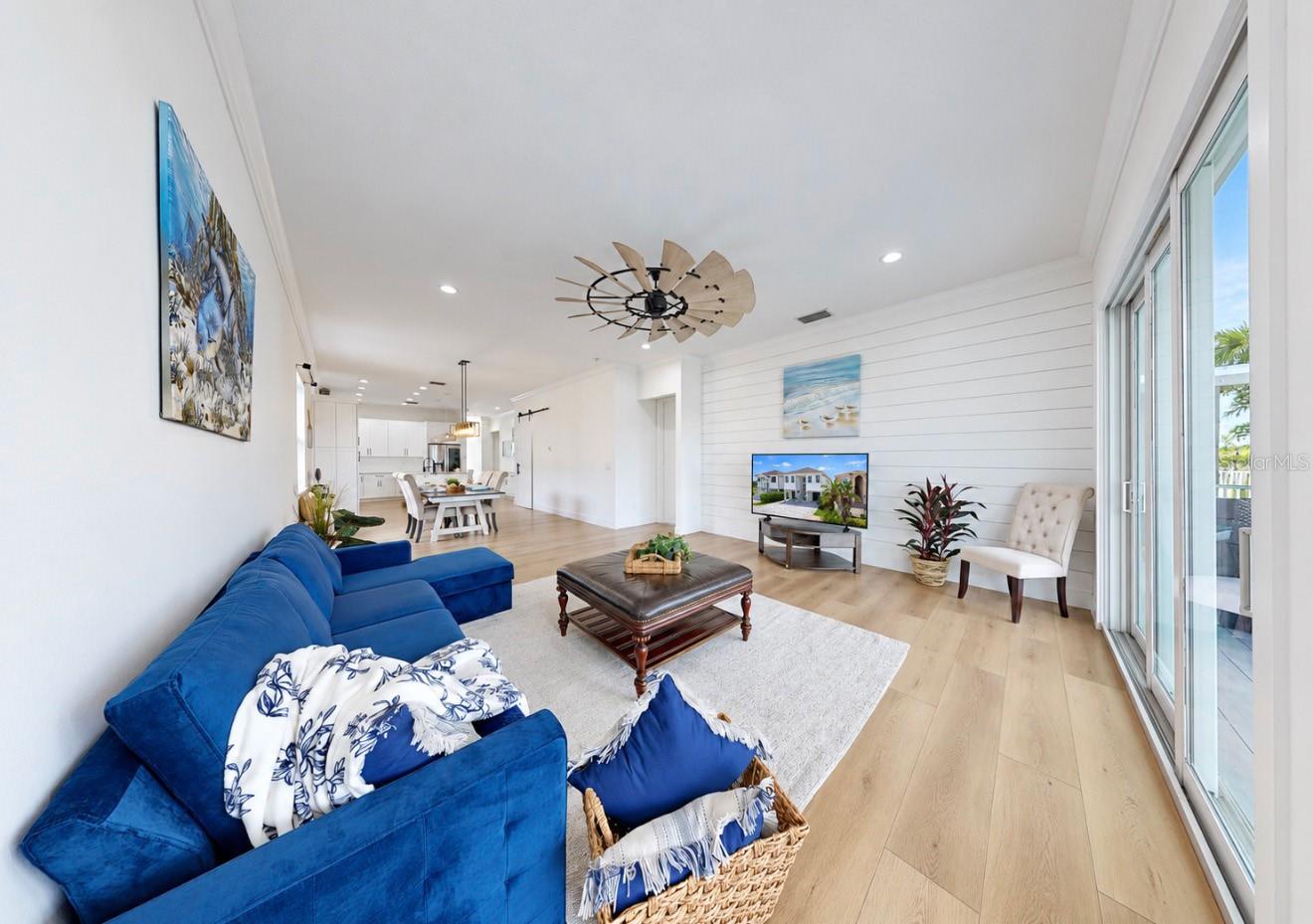 Open-plan living room with a blue sectional, white shiplap wall, and sliding glass doors.