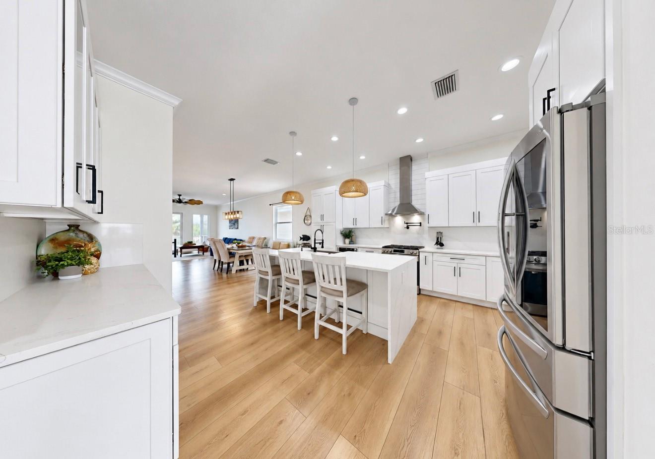 Open kitchen with a white island, stainless steel appliances, and light wood floors.