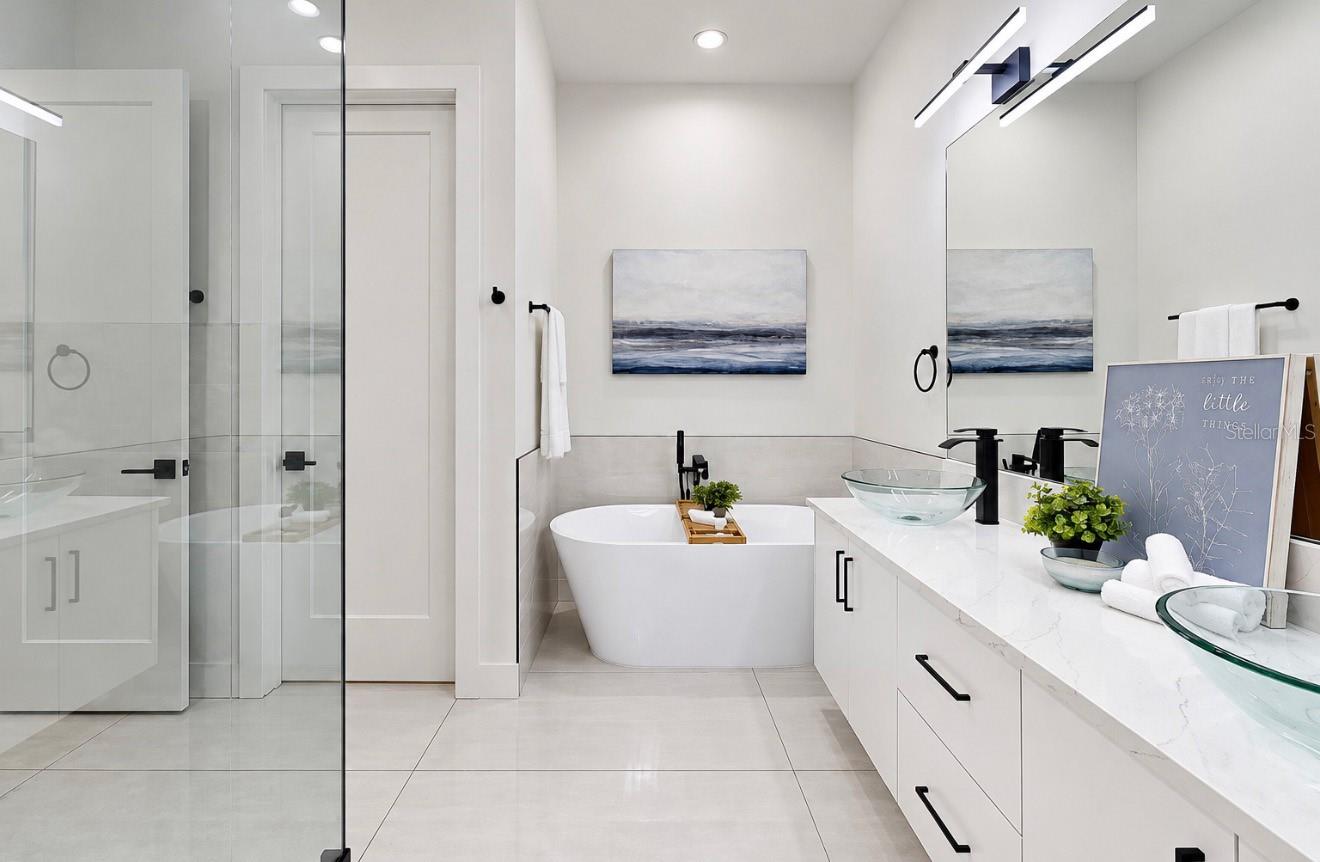 Staged bathroom with a freestanding tub, glass shower, and white double vanity with vessel sinks.