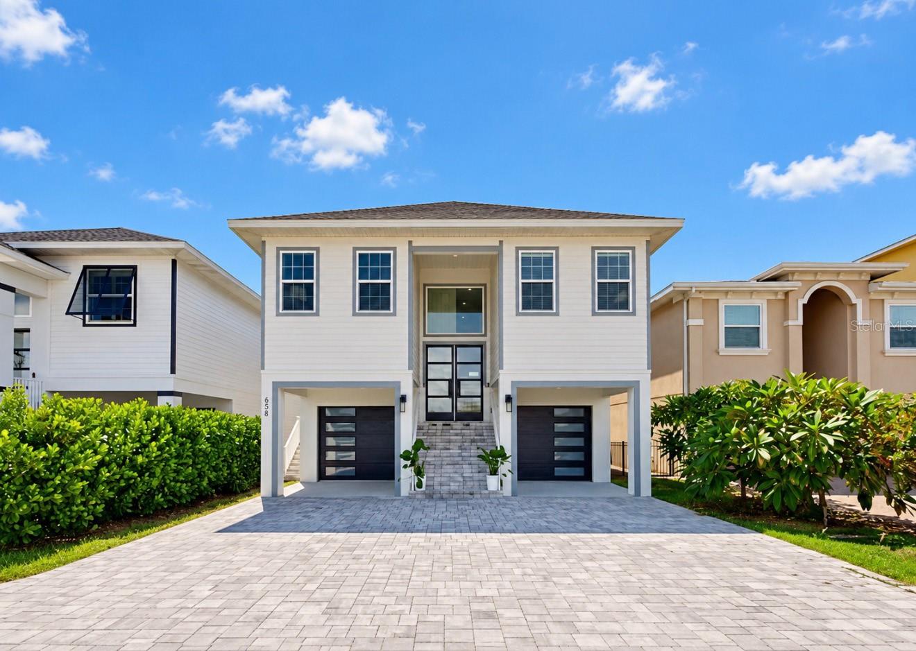 Two-story home with a central glass entry, twin garages, and a wide paver driveway.