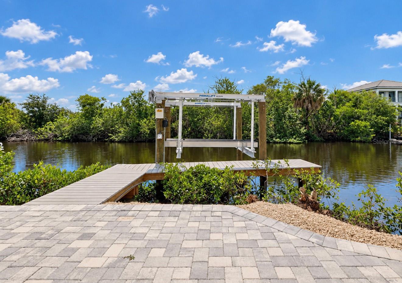 Waterfront dock with boat lift, paver patio, and mangroves along the canal.
