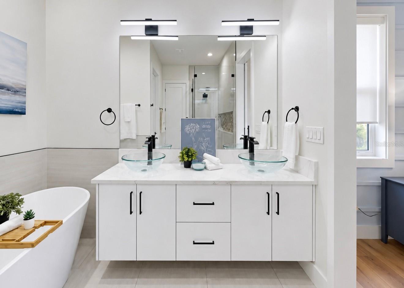 Bright bathroom with a double vanity, glass vessel sinks, and a freestanding soaking tub.