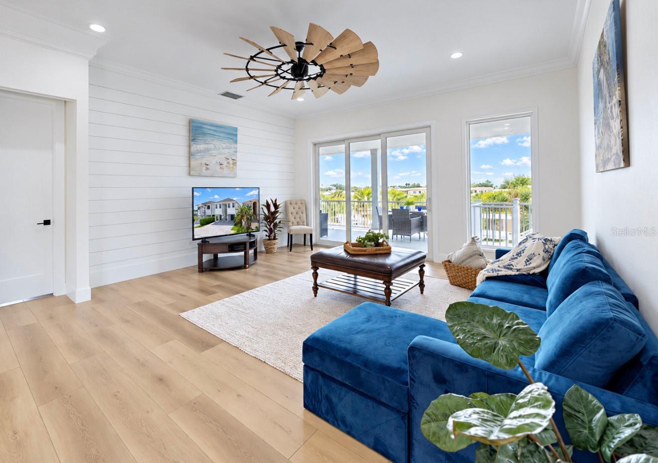 Living room with blue sectional, shiplap accent wall, and sliding doors overlooking water.