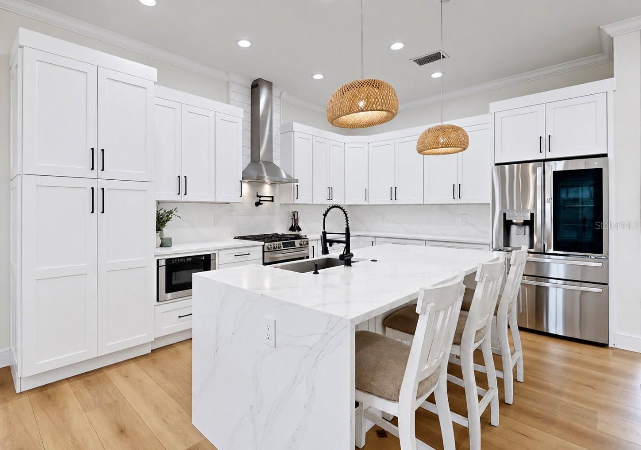 Modern white kitchen with a large marble-look island, stainless steel appliances, and woven pendant lights.