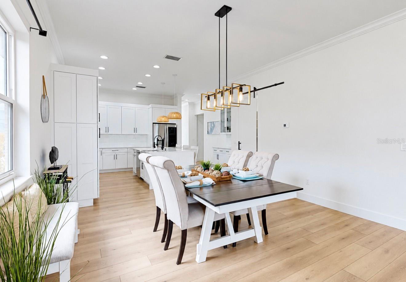 Open-plan dining room and kitchen with white cabinets, a dark table, and light wood floors.
