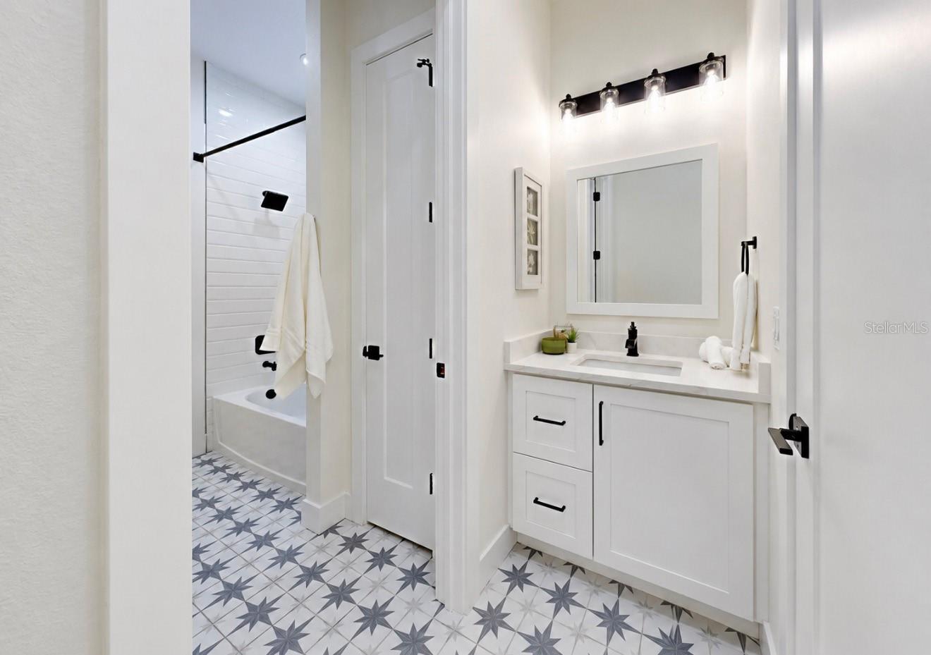 Bathroom with a white vanity and black fixtures, tub behind a glass panel, and star-patterned tile floor.