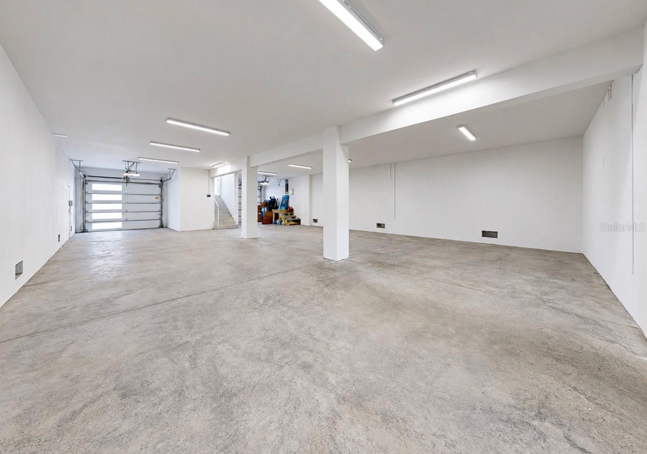 Spacious concrete-floor garage with fluorescent lighting, a sectional door, and stairs at the back.