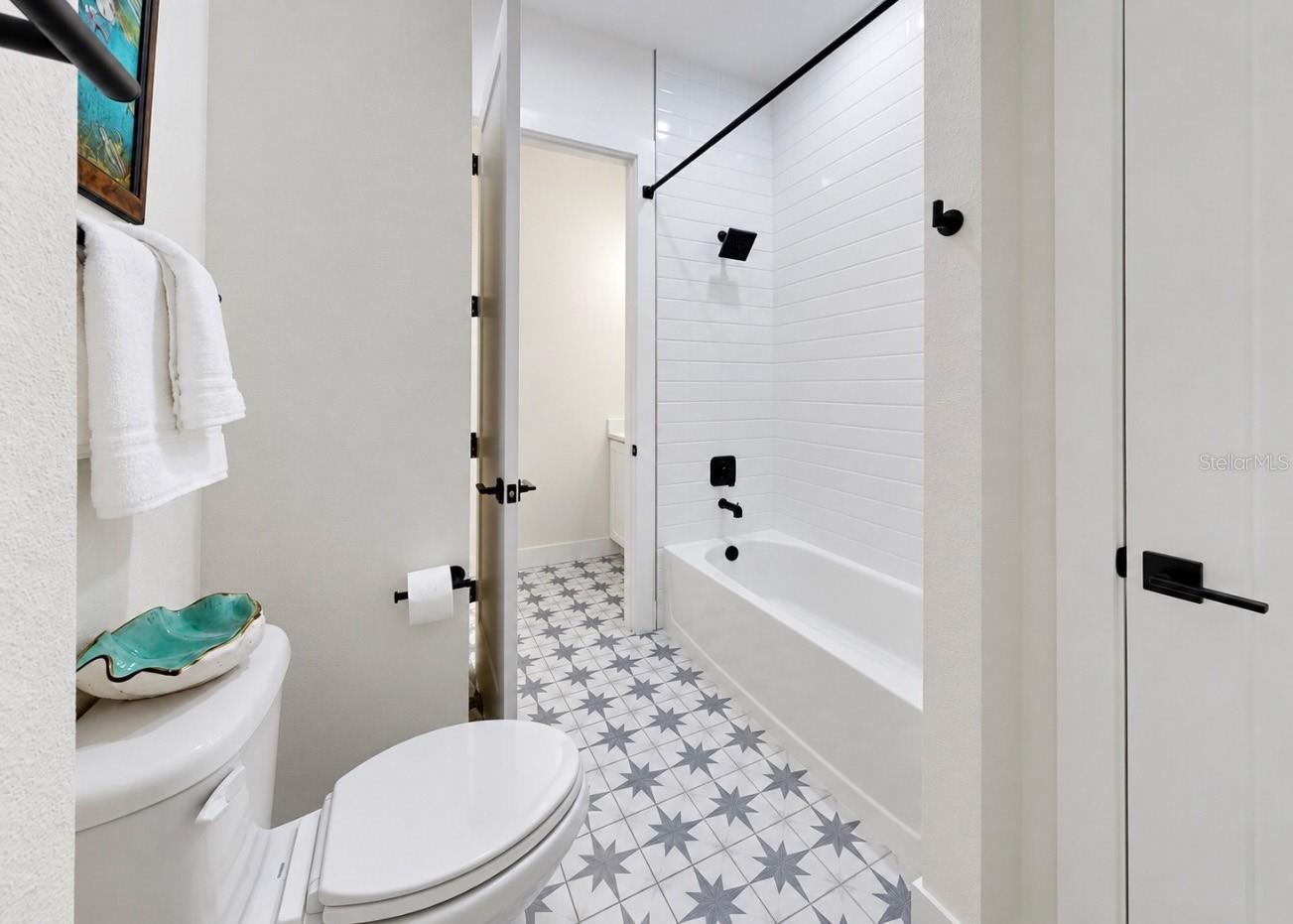 Bathroom with a white tub, black fixtures, and gray star-patterned floor tiles.