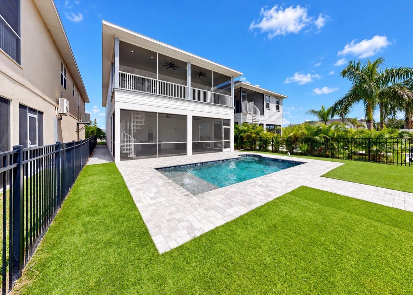 Modern two-story home with a covered balcony overlooking a paved backyard pool and lawn.