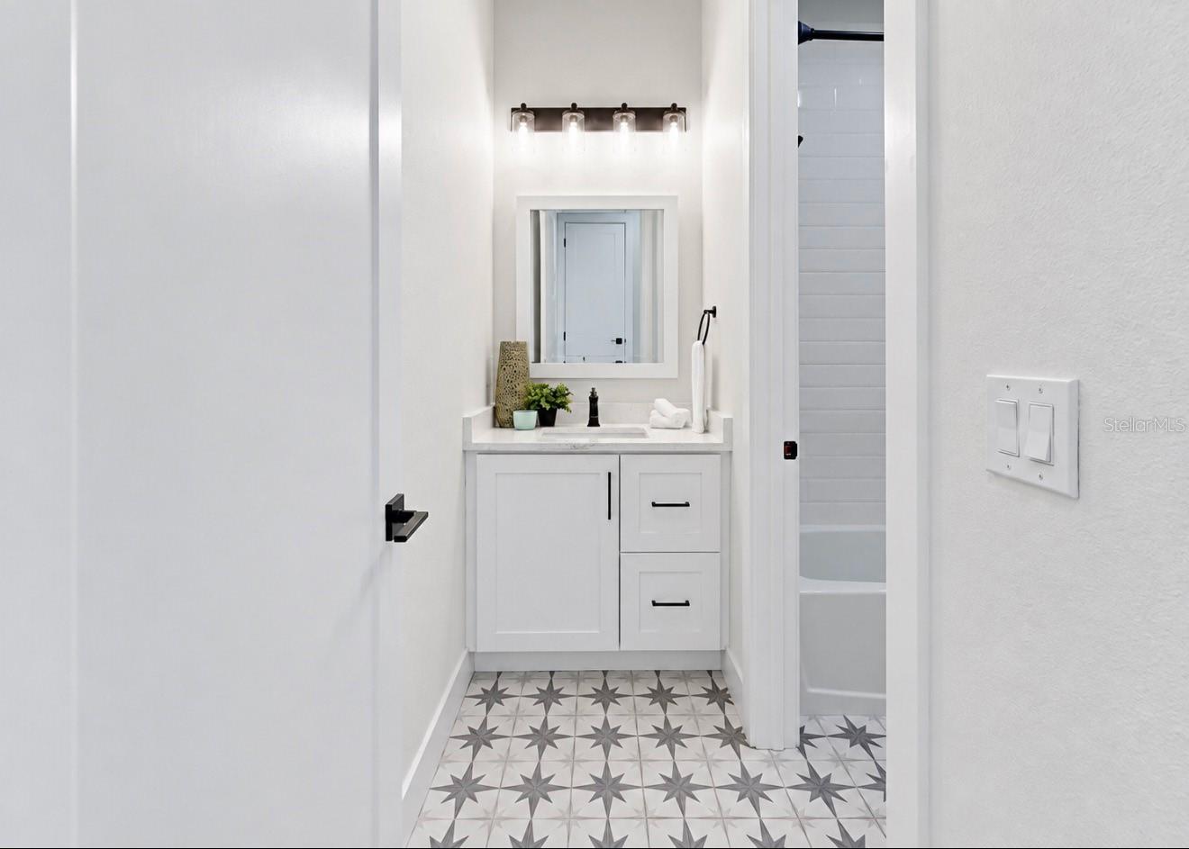 Bathroom with a white vanity and mirror, black fixtures, and distinctive gray star-patterned floor tile.