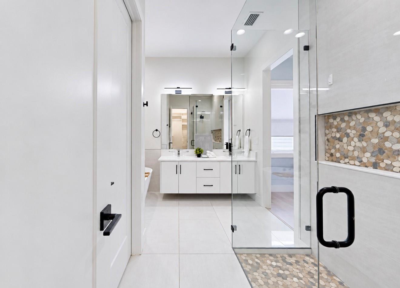 Bathroom with a white double vanity and glass shower with pebble-stone details.