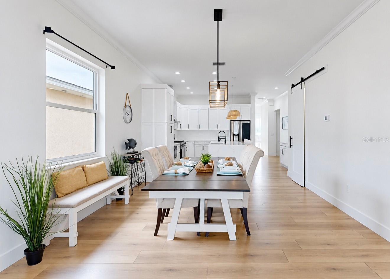 Open dining area with a set table, built-in bench, white kitchen, and light wood floors.