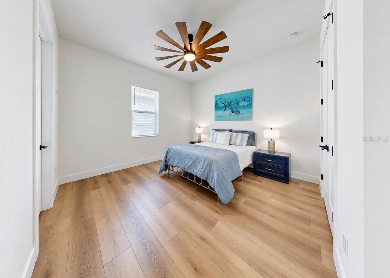Staged bedroom with pale blue bedding, fish artwork, navy nightstand, and light wood flooring.