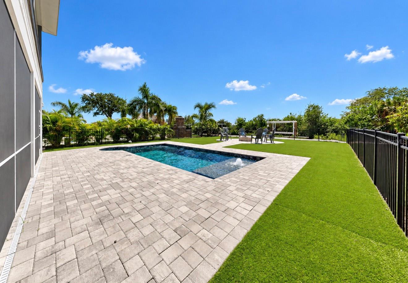 Backyard pool bordered by a wide paver patio and lawn, with palm trees and outdoor seating.