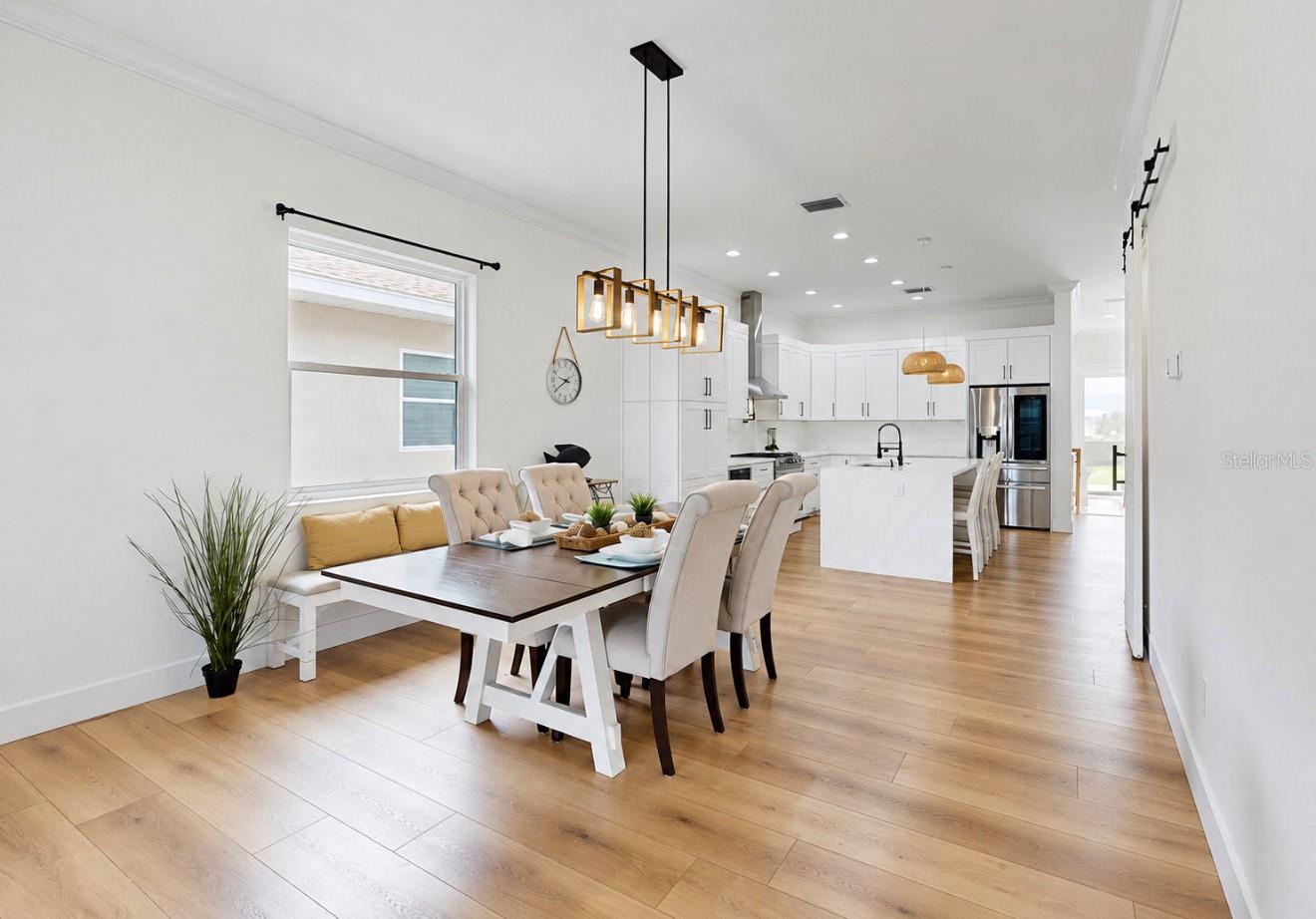 Dining area with a dark table and upholstered chairs beside a bright white kitchen and large island.