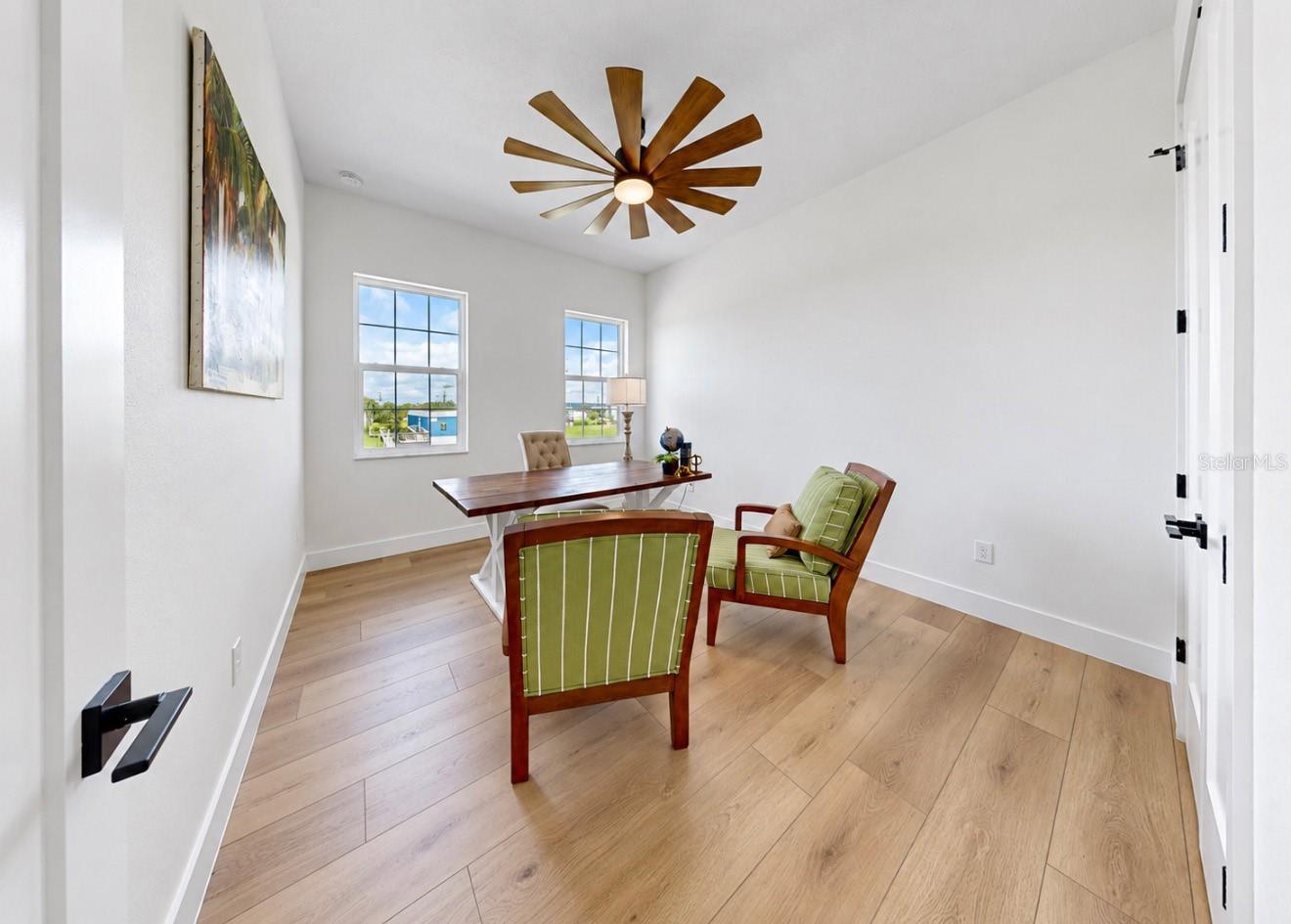 Dining room with a dark wood table, green chairs, light wood floors, and a large ceiling fan.