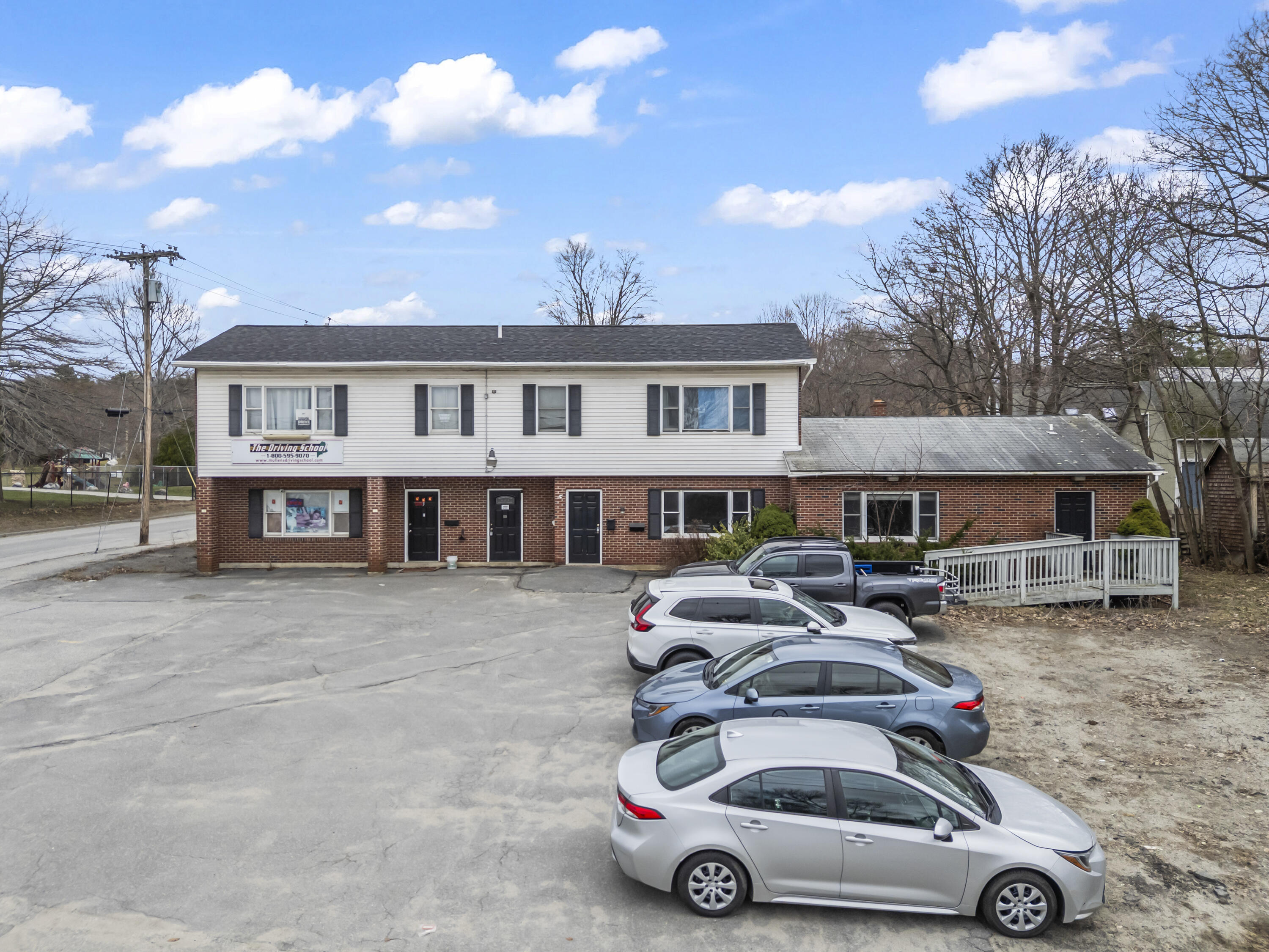 Two-story brick and white-sided commercial building with a parking lot and several parked cars.