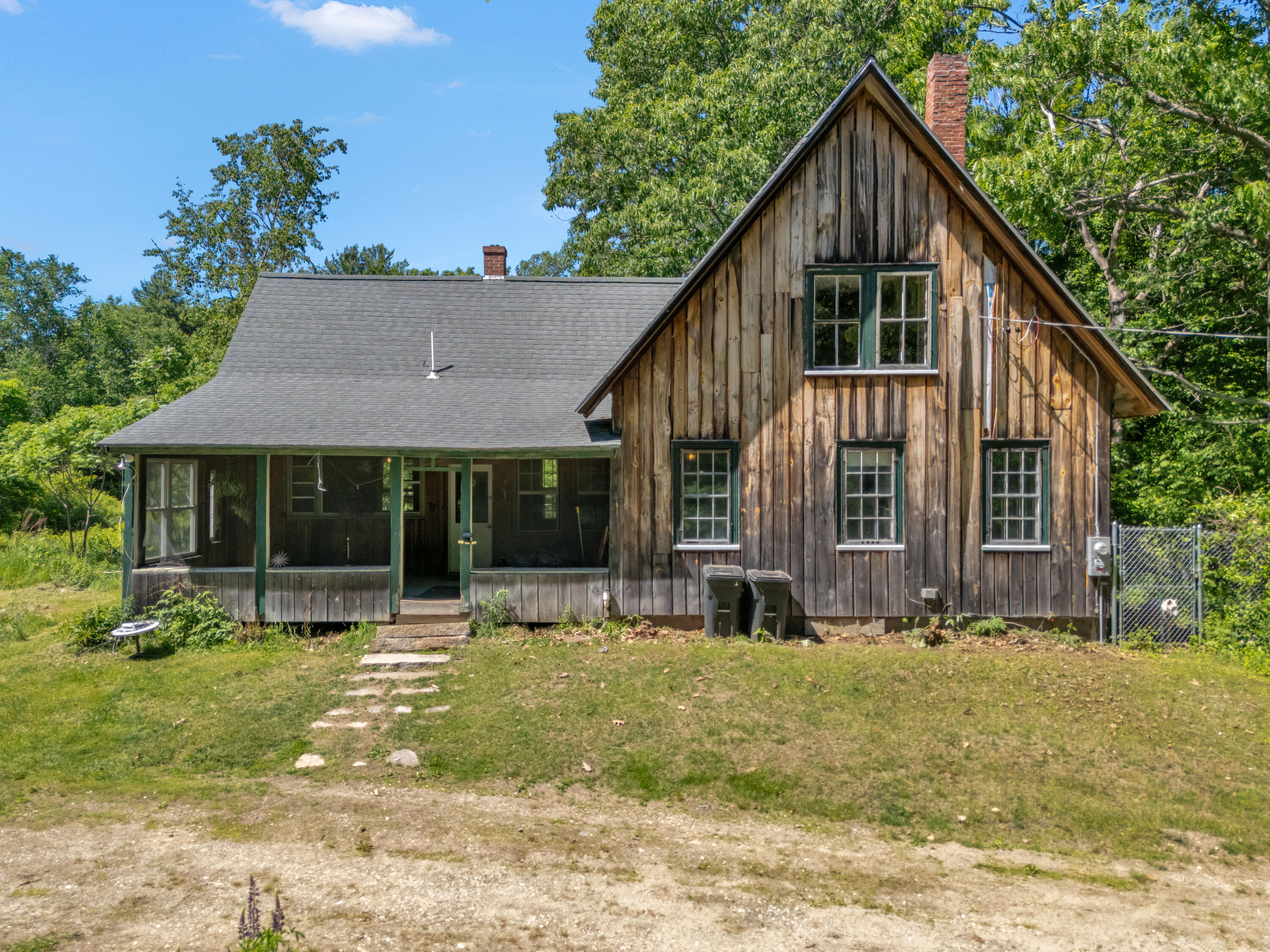 Rustic wood-sided home with a steep gable and covered porch among mature trees.
